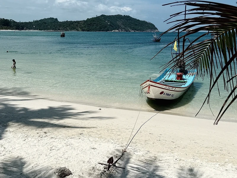 Weißer Strand mit Longtail-Boot, Palmen und türkisfarbenem Meer auf Koh Phangan